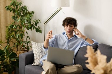 Mavi gömlekli yakışıklı bir adam çalışırken şık dairesinde telefonla konuşuyor..