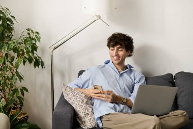 Kıvırcık saçlı şık bir genç, modern bir dairede, akıllı telefonunu kontrol etmekten zevk alır..