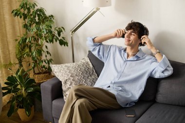 Kıvırcık saçlı yakışıklı genç bir adam şık dairesinde müzik dinlerken rahatlıyor..