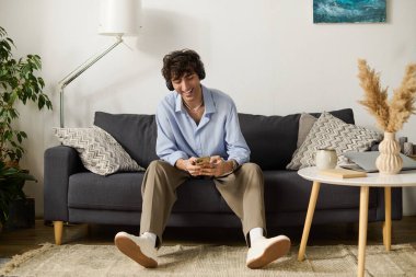 Yakışıklı kıvırcık genç adam modern bir ortamda telefonunu kontrol ederken koltuğunda dinleniyor..