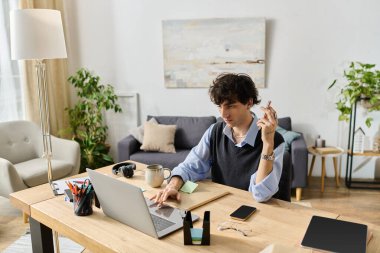 Kıvırcık saçlı genç adam, modern dekorlarla çevrili şık bir dairede dizüstü bilgisayarla çalışıyor..