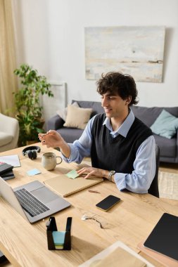 Kıvırcık saçlı genç adam modern dairesinde verimli bir iş gününün tadını çıkarıyor, gülümsüyor ve odaklanıyor..