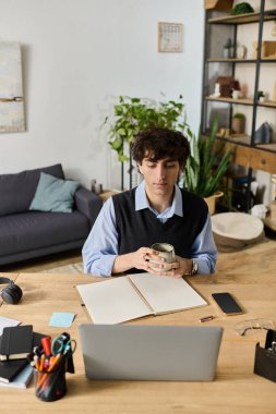 Kıvırcık saçlı yakışıklı genç adam masasında kahvesini yudumluyor..