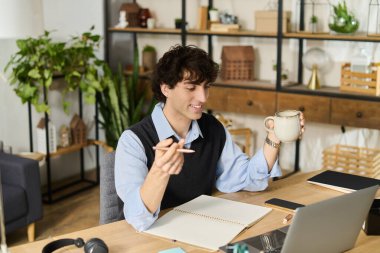 Kıvırcık saçlı genç adam şık masasında oturuyor, kahvesinin tadını çıkarıyor ve dairesinde notlar yazıyor..