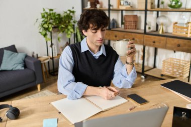 Kıvırcık saçlı genç, rahat bir dairede bir masada oturuyor, kahvesini yudumluyor ve fikirlerini düşünüyor..