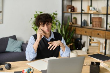 Şık mavi tişörtlü, kıvırcık saçlı genç adam rahat yaşam alanında telefonla konuşuyor..