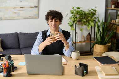 Genç adam mutlu bir şekilde telefonunu kullanıyor ve bitkilerle dolu yaşam alanında dinleniyor..