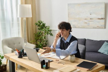 Mavi gömlekli yakışıklı bir genç modern dairesinde otururken telefonla konuşuyor..