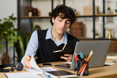 Kıvırcık saçlı yakışıklı genç bir adam modern dairesinde çalışırken defterine odaklanıyor..