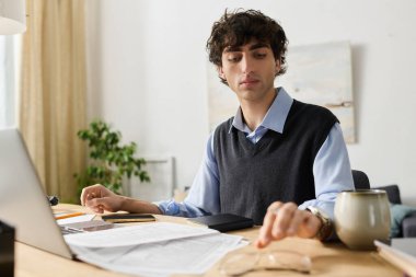 Mavi gömlekli şık genç adam şık dairesindeki görevlerine konsantre oluyor..