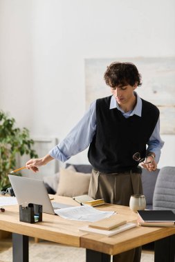 Mavi gömlekli genç adam şık dairesinde düşünceli bir şekilde duruyor, işine odaklanmış..