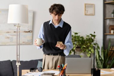 Yakışıklı genç bir adam şık dairesinde elinde kahveyle durup telefonuna bakıyor..