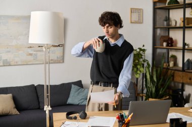 Mavi gömlekli genç adam modern yaşam alanındaki gazeteleri incelerken kahvenin tadını çıkarıyor..