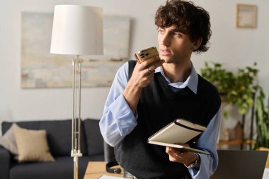 Modern dairesinde kıvırcık saçlı yakışıklı genç adam elinde bir defter tutuyordu..
