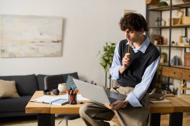 Şık bir genç adam, gündelik giyinmiş, ahşap bir masada oturur ve dizüstü bilgisayarında fikirler düşünürken....