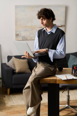 Kıvırcık saçlı genç adam, modern, şık bir apartman ortamında dizüstü bilgisayarına odaklanıyor..