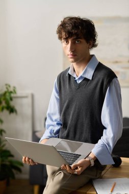 Kıvırcık saçlı genç adam modern bir dairede dizüstü bilgisayarla rahatça oturur, derin düşüncelere dalmış..