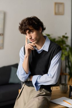 Kıvırcık saçlı yakışıklı bir genç adam şık dairesinde düşünceli bir şekilde yansıyor..