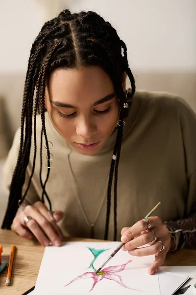 Saçları örgülü genç bir Afrikalı Amerikalı kadın rahat evinde canlı bir çiçek çizmeye odaklanıyor..