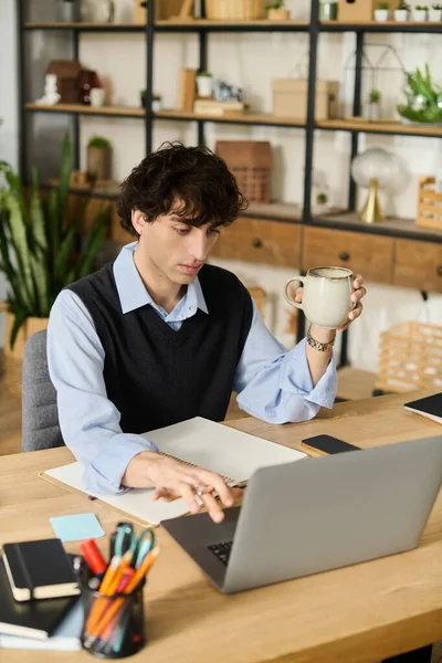 Şık genç adam rahat bir apartman dairesinde dizüstü bilgisayarıyla çalışırken bir şeyler içmekten hoşlanıyor..