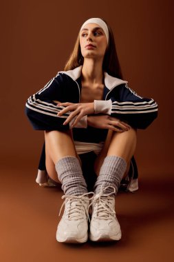 Spor kıyafetleri içinde fit bir genç kadın sıcak kahverengi bir arka plana karşı güvenle poz verir..