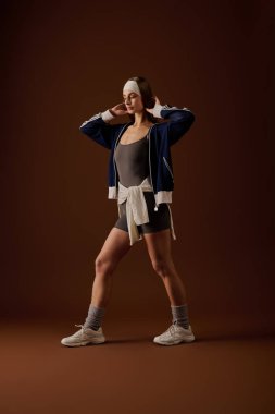 Genç bir kadın kendine güvenerek spor kıyafetleriyle poz veriyor, atletik tarzını vurguluyor..