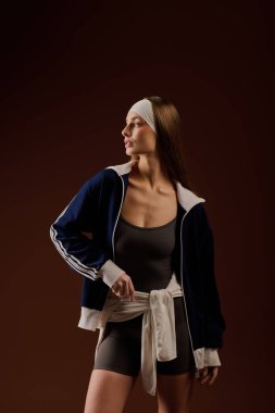 Genç, atletik bir kadın sıcak kahverengi bir arka plana karşı güvenli bir şekilde spor kıyafetleriyle poz veriyor..