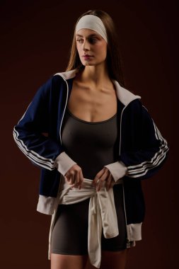 Formda genç bir kadın şık spor kıyafetleri ve şık kahverengi bir stüdyoda saç bandı sergiliyor..