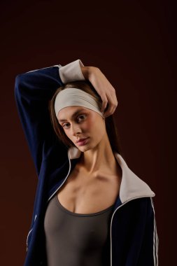 Kahverengi bir stüdyoda atletizm tarzını sergileyen genç bir kadın kendine güveni ve soğukkanlılığıyla.