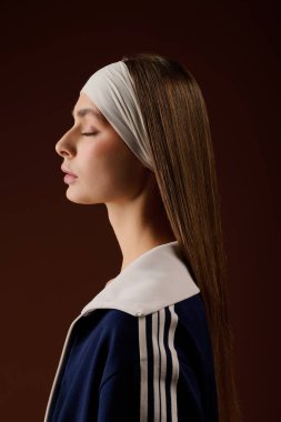 Formda genç bir kadın spor kıyafetleri içinde zarif bir şekilde poz verir. Sıcak bir stüdyoda atletizm tarzını benimser..