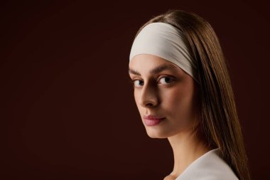 Şık spor kıyafetleri içinde kendine güvenen genç bir kadın kahverengi bir stüdyoda zarif bir şekilde duruyor..