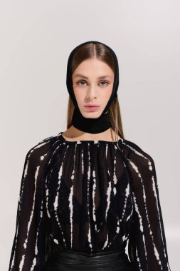 Gri bir stüdyoda zarif giysilerini sergileyen güzel bir genç kadın..