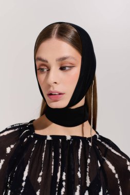 Gri bir stüdyoda şık bir saç bandıyla şık bir şekilde poz veren hoş bir genç kadın..