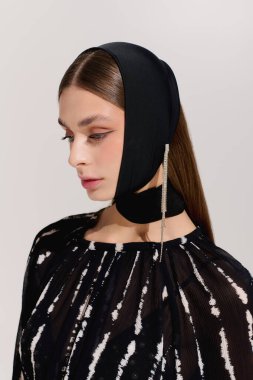 Genç bir kadın, minimalist gri bir stüdyoda zamansız bir şekilde poz verir..