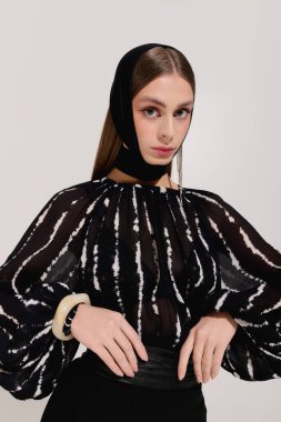 Zarif giyinmiş genç bir kadın zarif bir şekilde gri bir stüdyoda poz veriyor..