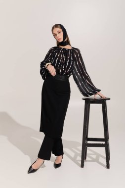 Genç bir kadın zarif tarzını gri bir stüdyoda, şık bir saç bandıyla gösteriyor..