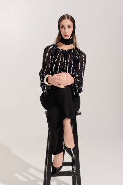 Şık giyinmiş genç bir kadın zarif bir şekilde modern gri bir stüdyoda poz veriyor..