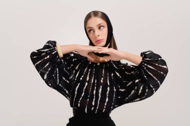 Zarif giyinmiş zarif genç bir kadın gri bir stüdyo arkaplanına zarif bir şekilde poz veriyor..