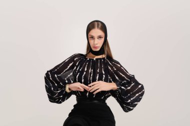 Zarif genç bir kadın, moda tarzını gri bir stüdyo ortamında sergiliyor..