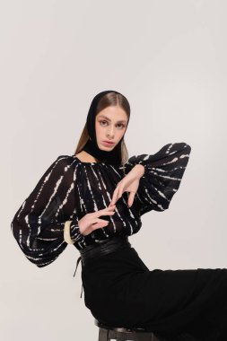 Zarif giyinmiş zarif genç bir kadın zarif bir şekilde gri bir arkaplanda poz veriyor..