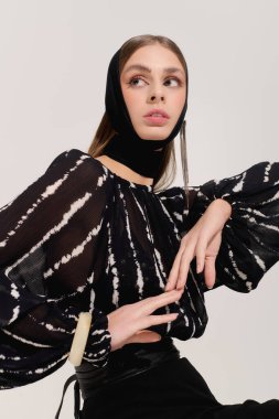 Güzel genç bir kadın zarif bir şekilde poz verir. Gri bir stüdyoya güven saçar..