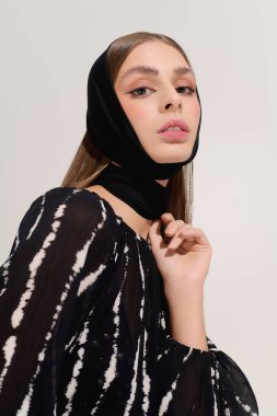 Modayı takip eden genç bir kadın, şık kıyafetini gri bir arka planda sergiliyor..