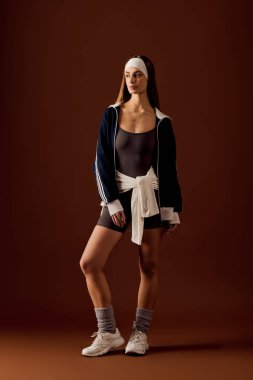 Atletik kadın spor tarzını ve özgüvenini şık kahverengi bir stüdyoda sergiliyor..