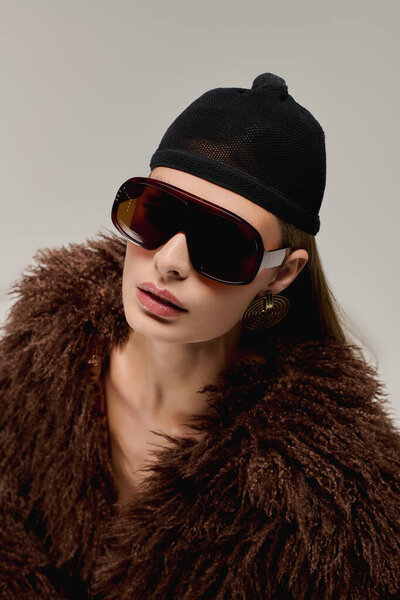A stylish young woman confidently poses in a faux fur jacket and chic sunglasses.