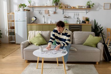 Genç adam, sıcak, davetkar bir yaşam alanında bir yapboz üzerinde çalışarak rahatlatıcı bir öğleden sonranın tadını çıkarıyor..