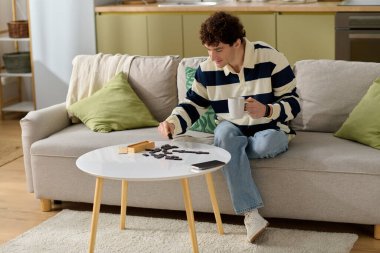 Yakışıklı genç adam bir kanepede rahatça oturur, bir oyunda kahvesini yudumlarken..