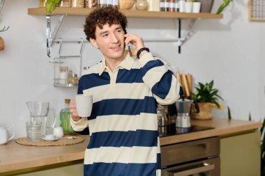 Gülümseyen genç bir adam şık bir mutfakta içki içerken telefon eder..