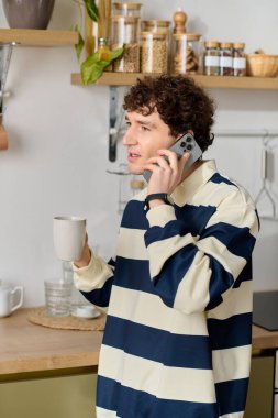 Çizgili elbiseli yakışıklı genç bir adam mutfakta sıcak bir içki yudumlarken bir telefon görüşmesi yapıyor..