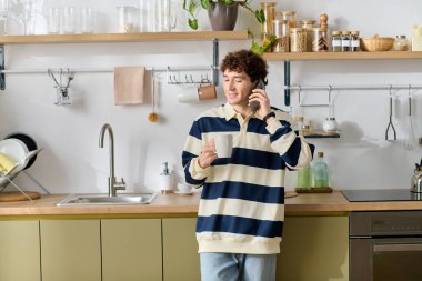 Genç adam şık bir mutfakta kahvesini yudumluyor, telefonda gevşek ve neşeli bir şekilde sohbet ediyor..