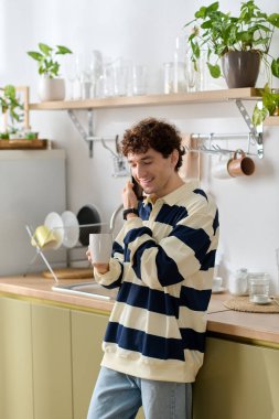 Yakışıklı genç adam yeşil bir mutfakta kahvesini yudumlarken gülümsüyor..